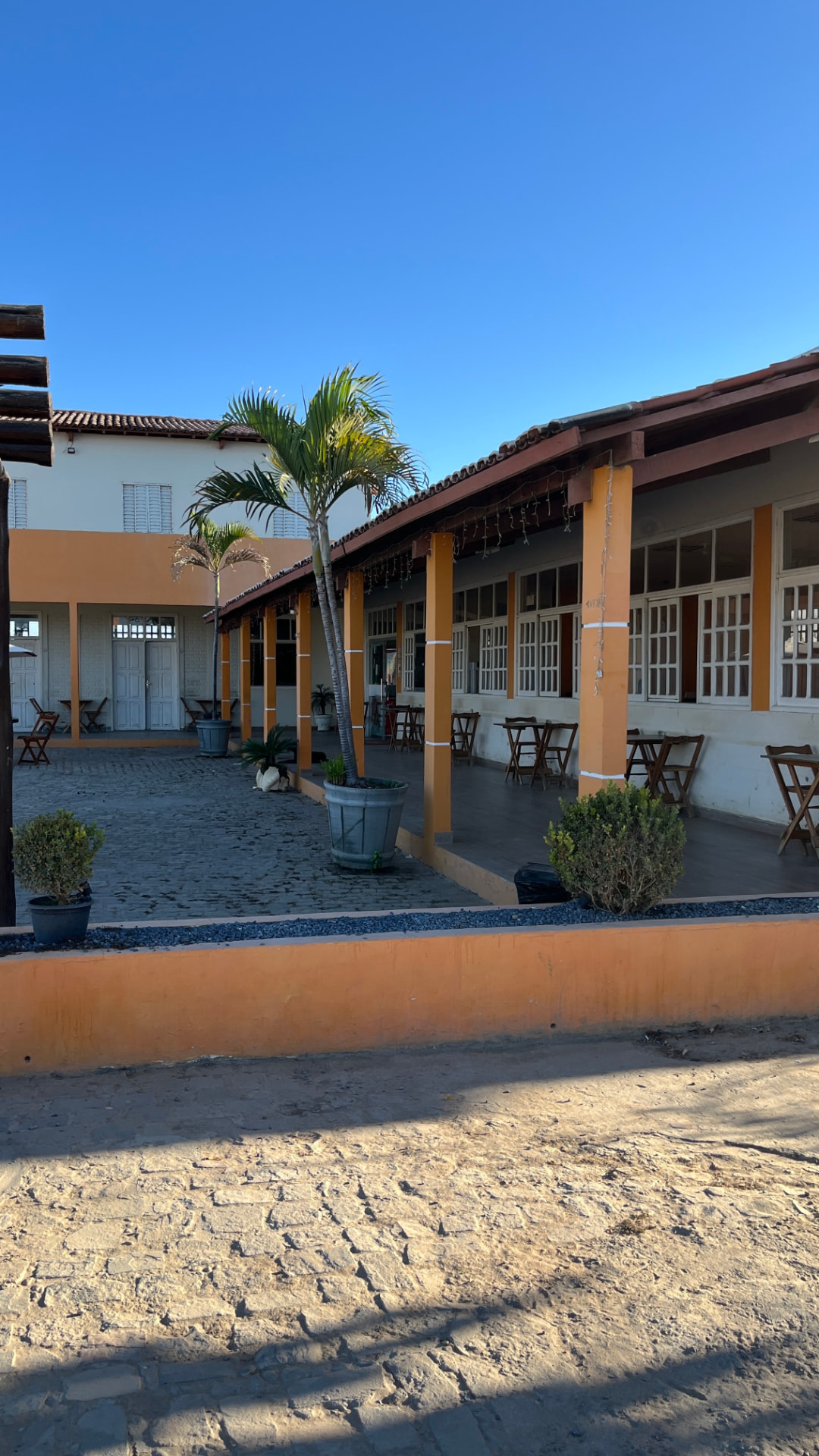 Área externa com palmeiras, jardim e varanda do restaurante e pousada