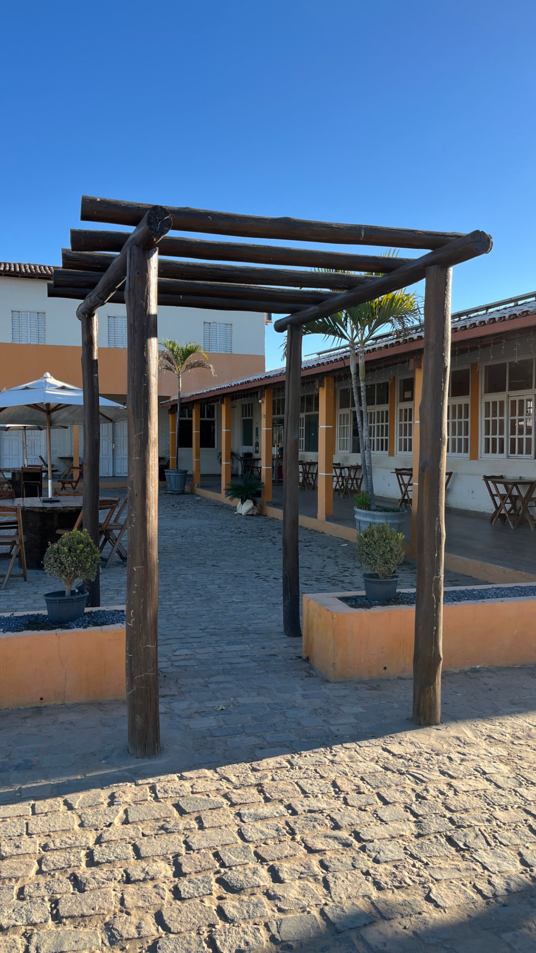 Pergolado de madeira na entrada do pátio com ombrelones e mesas