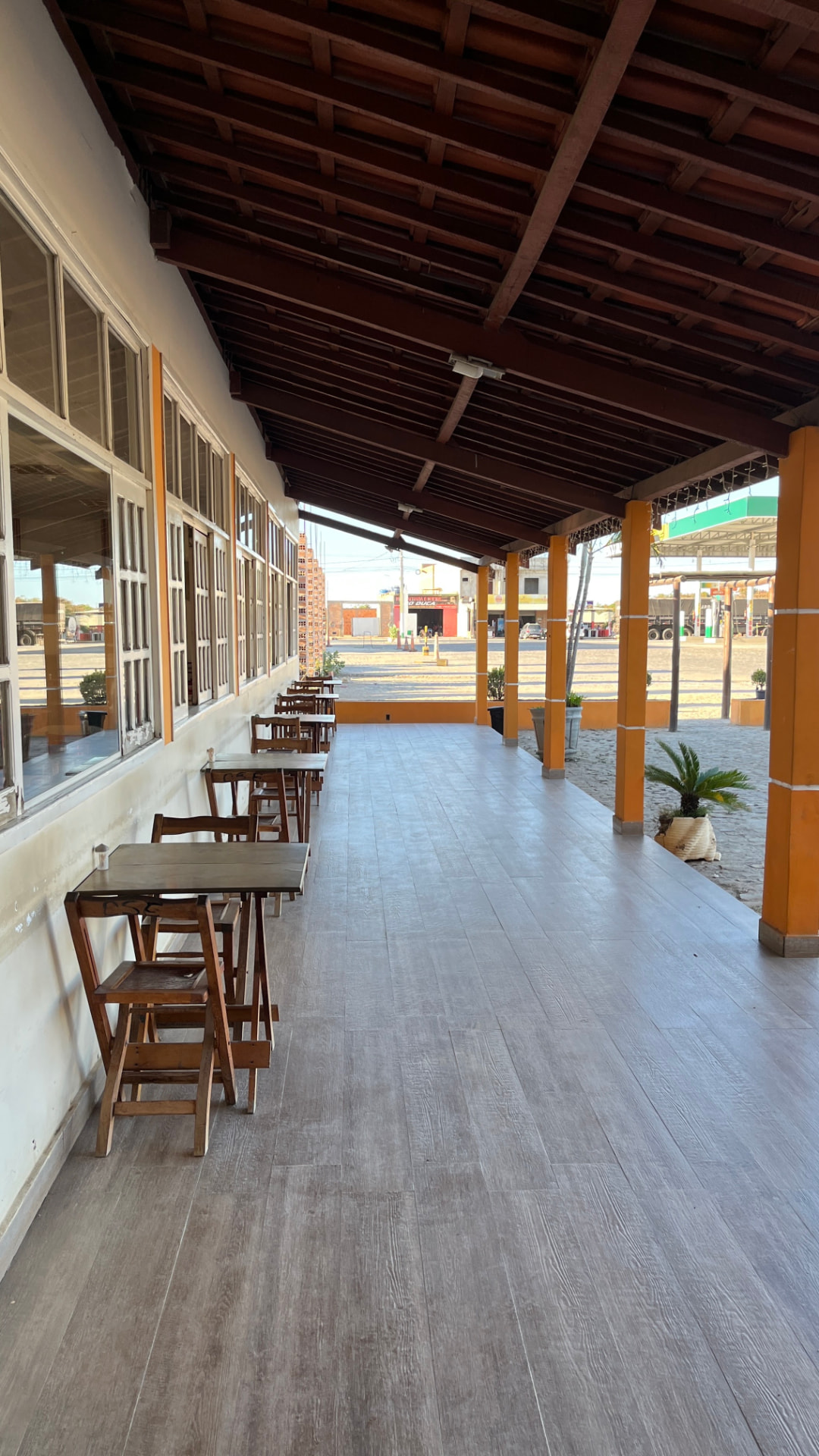 Varanda coberta com mesas de madeira ao lado do salão do restaurante